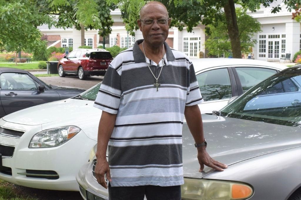 Patient Darryl stands in the parking lot, touching his car
