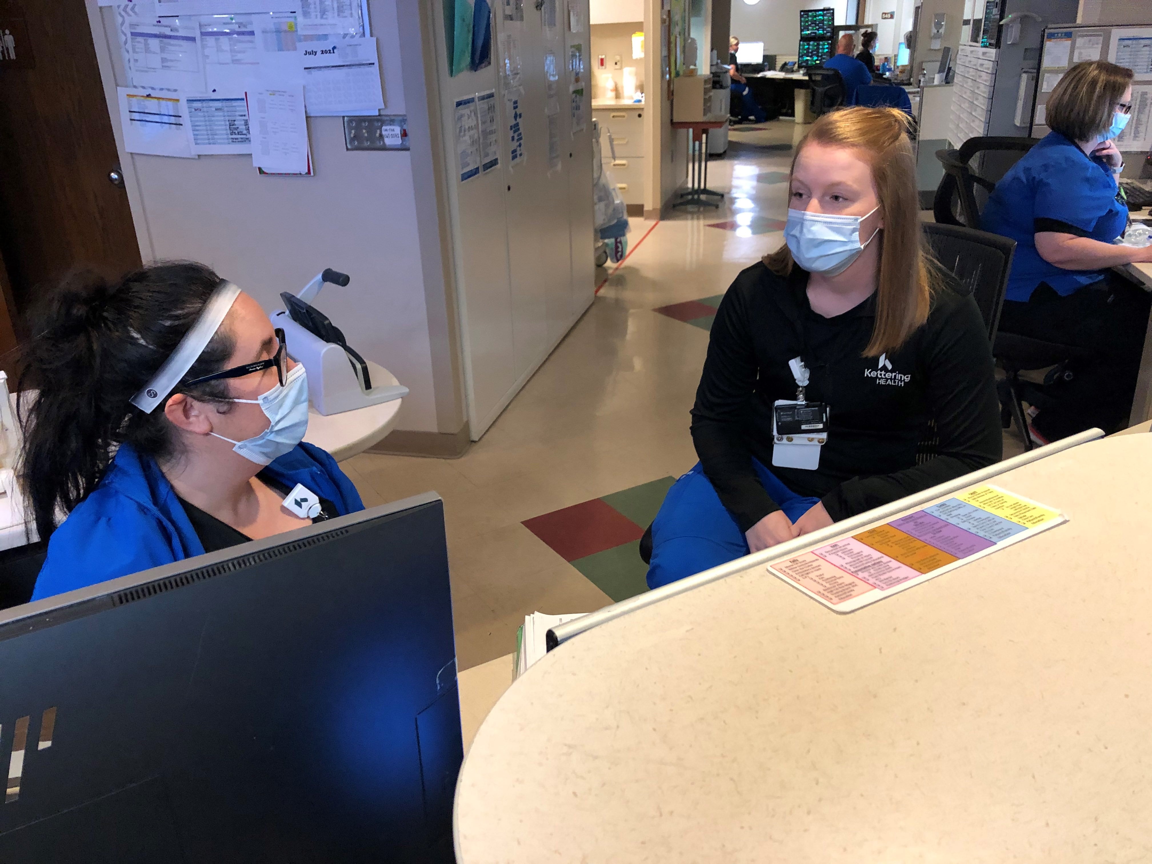 Young nurse sits with coworker talking with masks